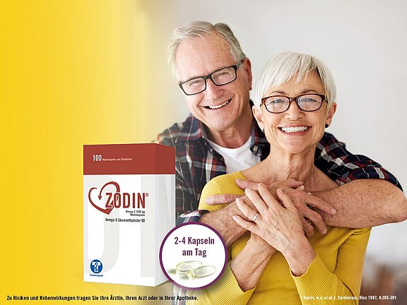 Ein lächelndes älteres Ehepaar umarmt sich neben einer Schachtel mit Zodin-Kapseln, auf der 2-4 Kapseln pro Tag empfohlen werden.
