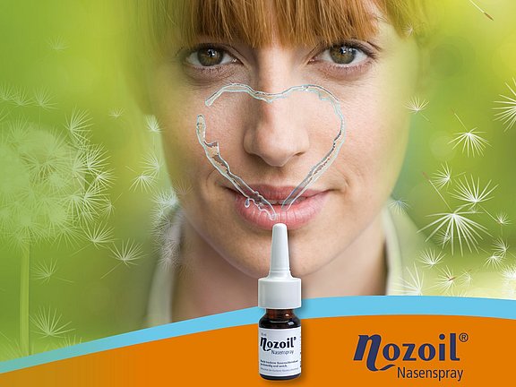 Frau von vorne mit einem Herz aus Nozoil-Flüssigkeit um die Nase, das aus der Sprayflasche austritt. Im Hintergrund befinden sich mehrere verblasste Löwenzahnblumen vor grünem Hintergrund.